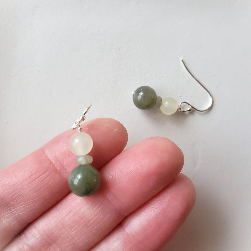 Pair of earrings with green and white beads held between fingers on a light background