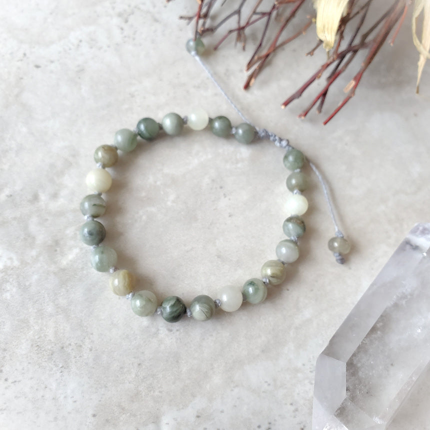 Beaded bracelet on a textured surface with a crystal and branches in the background