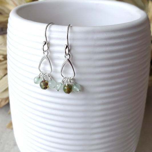 Silver earrings with green beads hanging from a white ceramic cup.