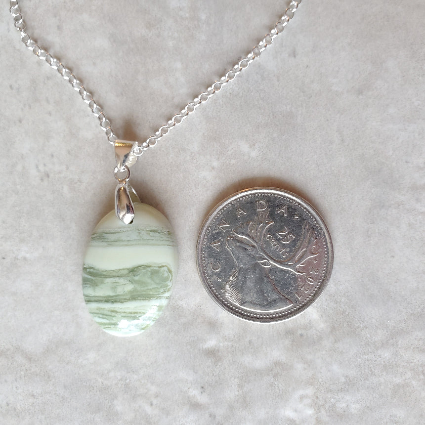 Serpentine oval pendant necklace beside a quarter