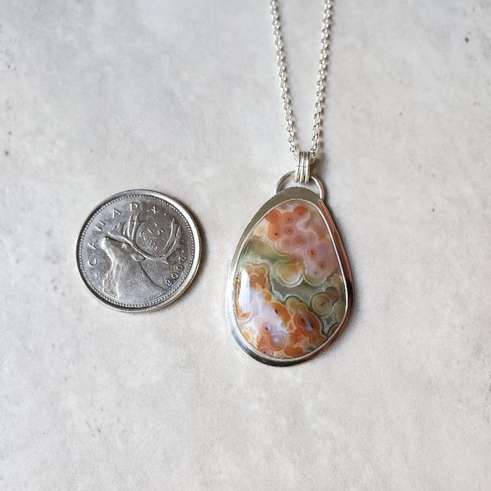 Ocean Jasper Freeform silversmith pendant beside a quarter