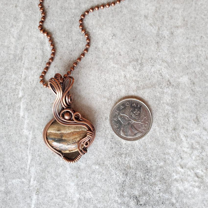 Aragonite wire wrap pendant beside a quarter