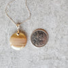 Banded Agate round pendant necklace beside a quarter