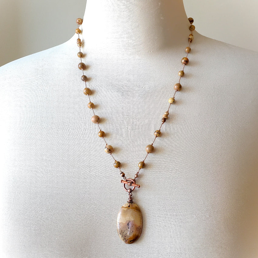 Necklace with brown beads and a large pendant on a mannequin.
