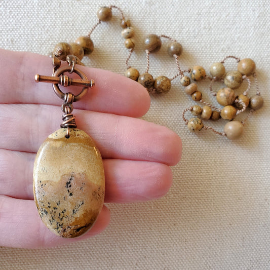 Necklace with a large pendant held by a hand on a beige fabric background