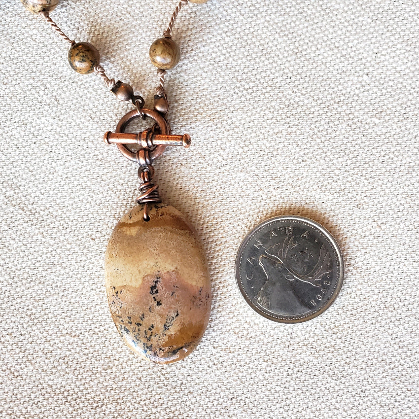 Necklace with a large brown pendant next to a Canadian quarter on a textured fabric background