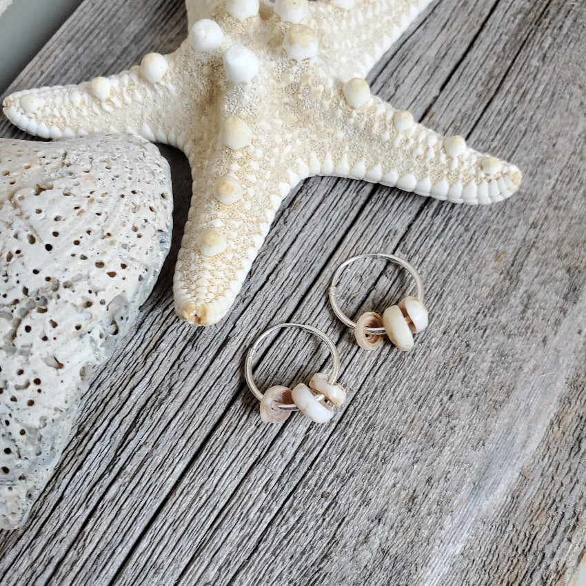 Pair of shell earrings on a wooden surface with starfish and shell in the background