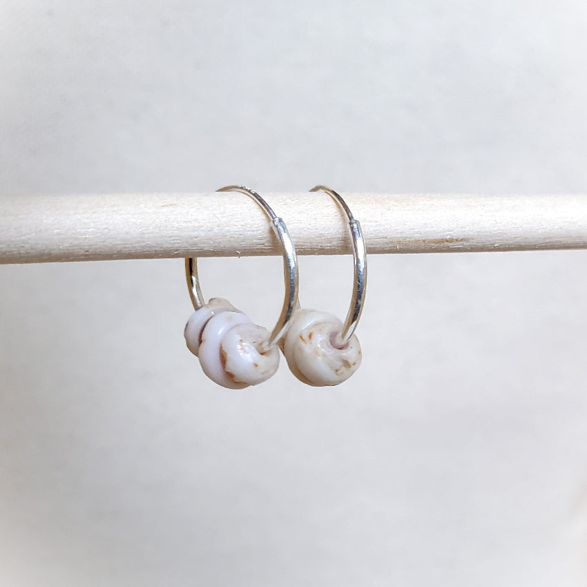 Pair of silver hoop earrings with shell-like beads on a white background