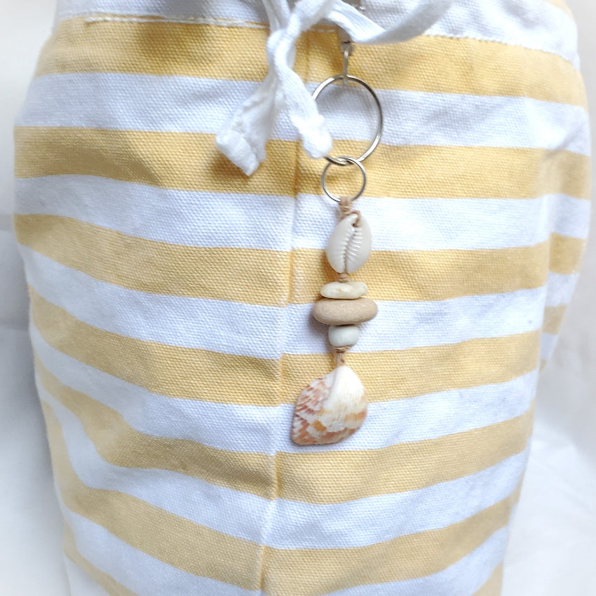 Yellow and white striped bag with a keychain featuring seashells on a white background