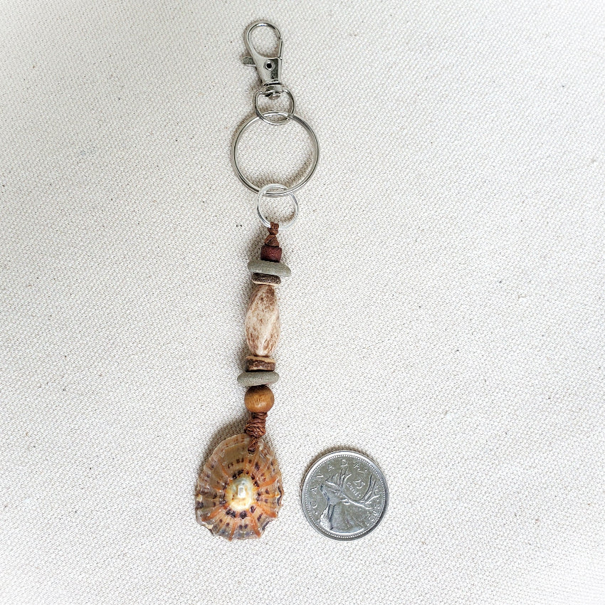 Keychain with shell and bead design next to a quarter for scale on a white background