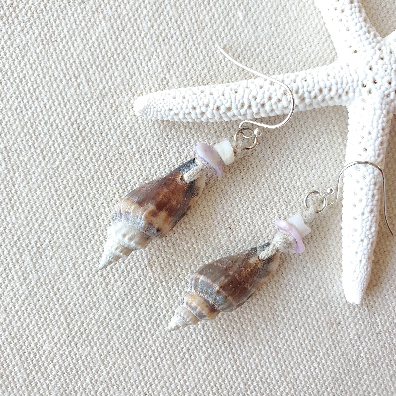 Shell-shaped earrings with pink beads on a textured surface