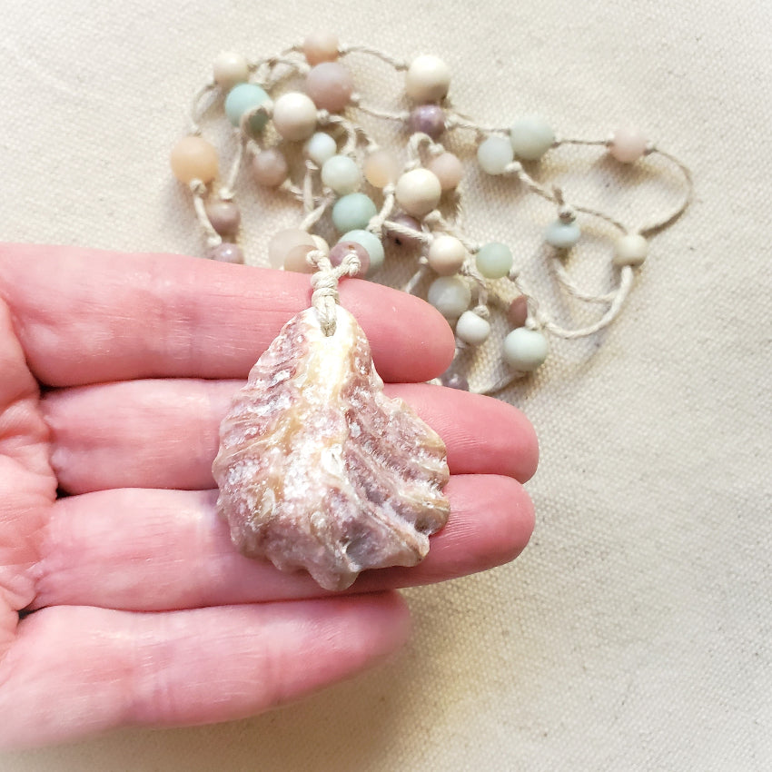 Hand holding a shell pendant with a necklace of gemstones in the background