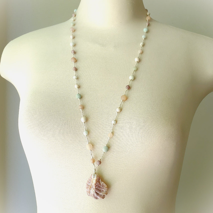 Necklace with a shell pendant on a mannequin against a neutral background