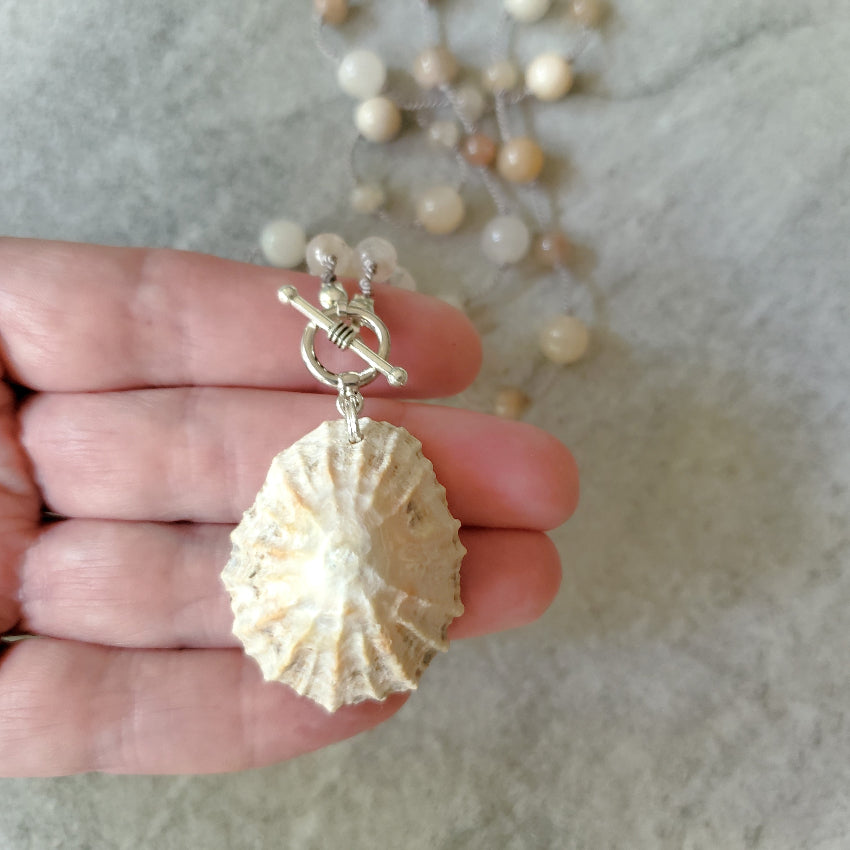 Shell pendant on a necklace held in a hand against a neutral background