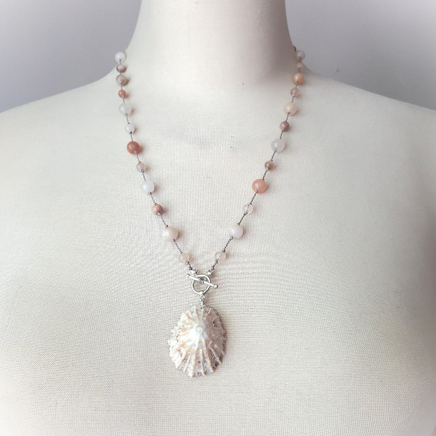 Necklace with shell pendant on a mannequin against a neutral background