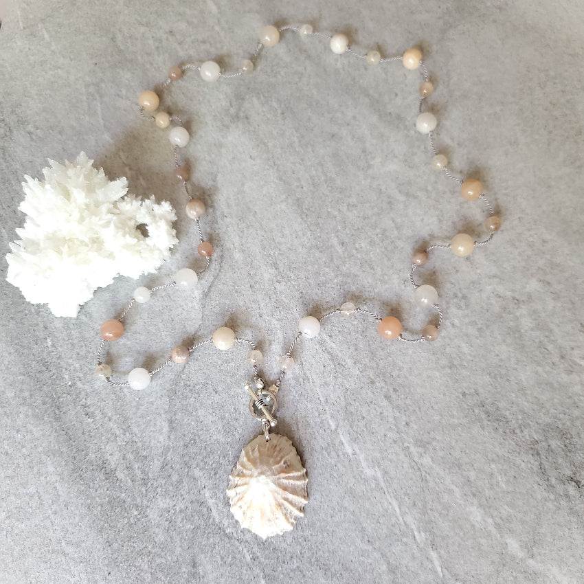 Pearl necklace with a silver shell pendant on a textured gray surface