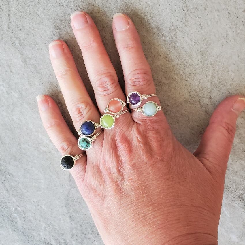 Hand wearing multiple rings with colorful gemstones on a neutral background