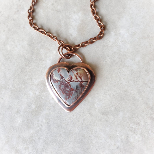 Copper heart-shaped necklace with a natural stone pendant on a light gray background