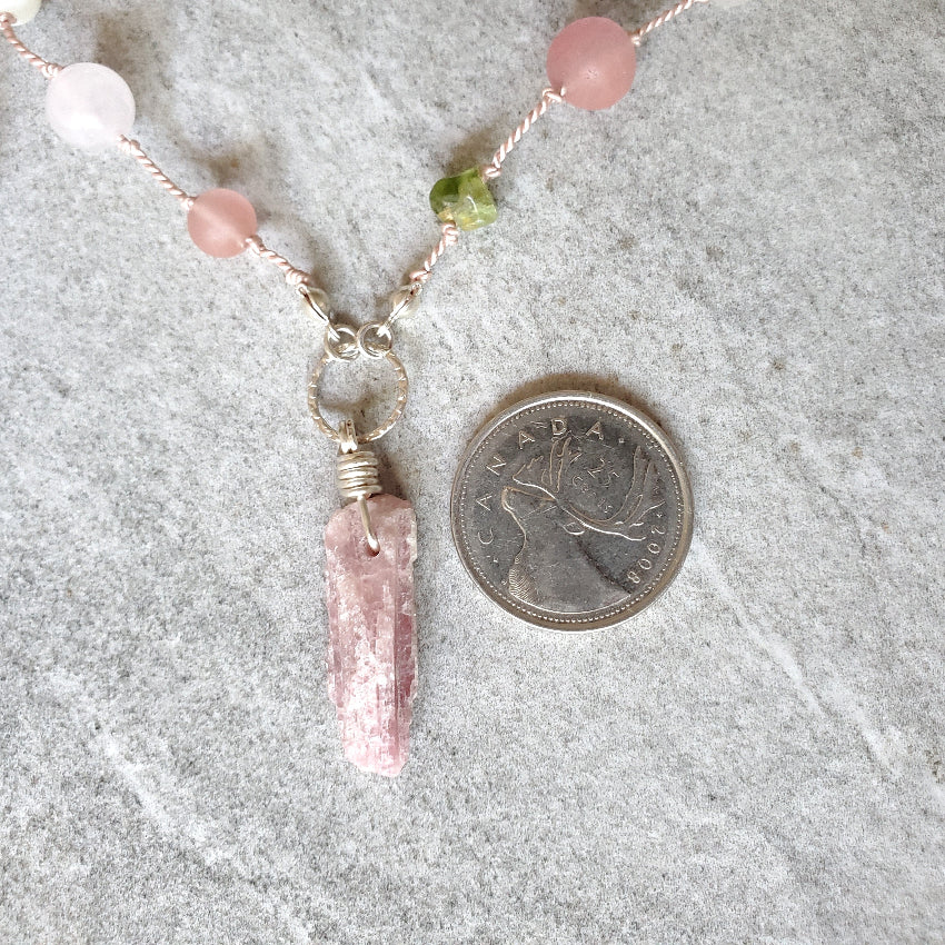 Necklace with a pink Tourmaline pendant next to a Canadian quarter on a gray surface