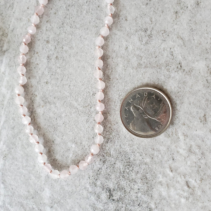 Faceted Rose Quartz knotted necklace beside a quarter