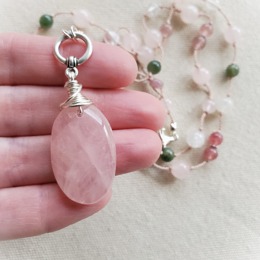 Pink stone pendant on a silver chain held by a hand with a blurred background