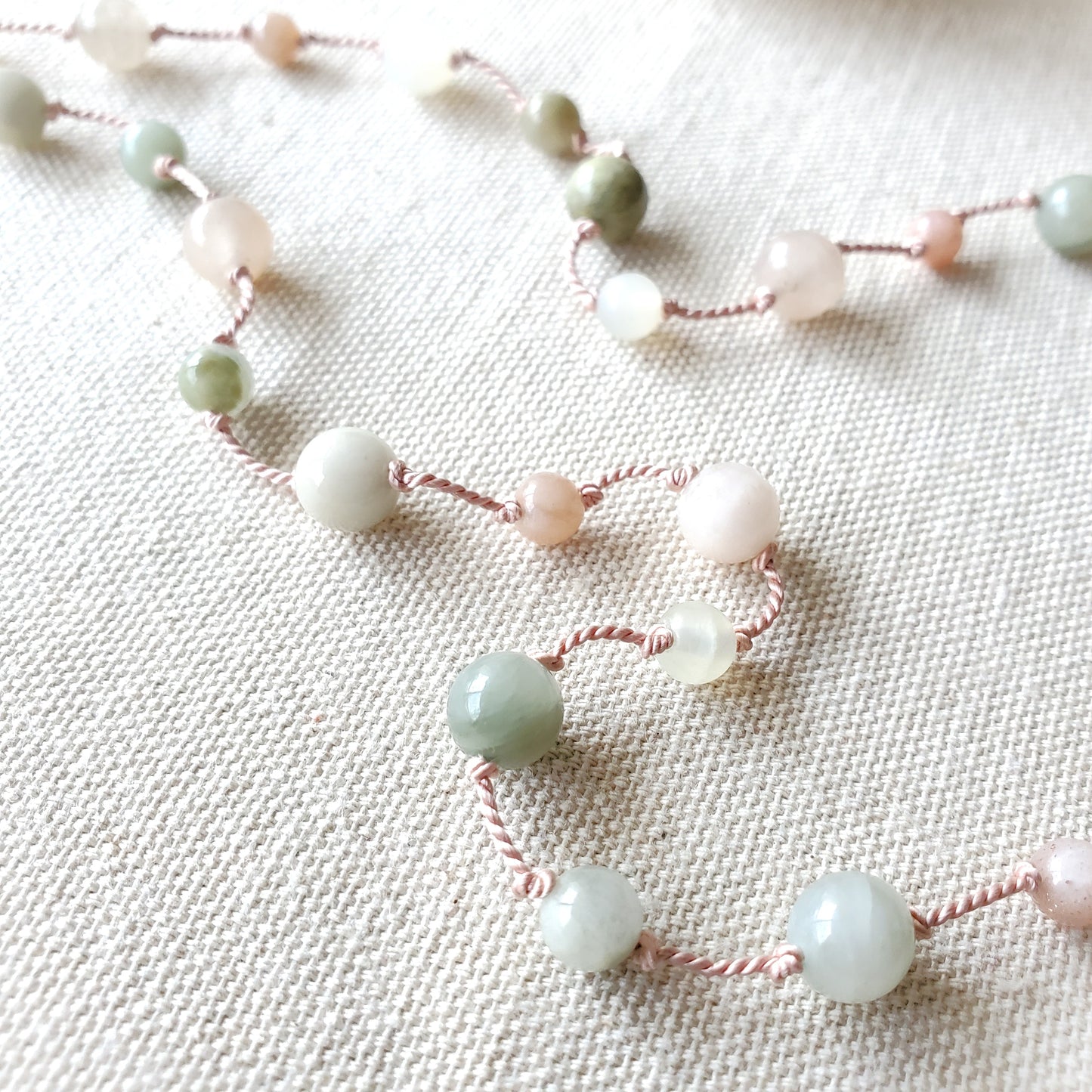 String of light green and pink beads on a textured fabric background