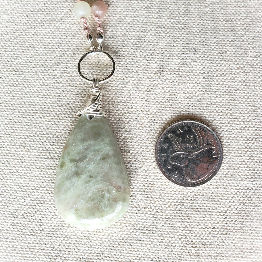 Pendant with a teardrop-shaped green stone on a textured fabric background