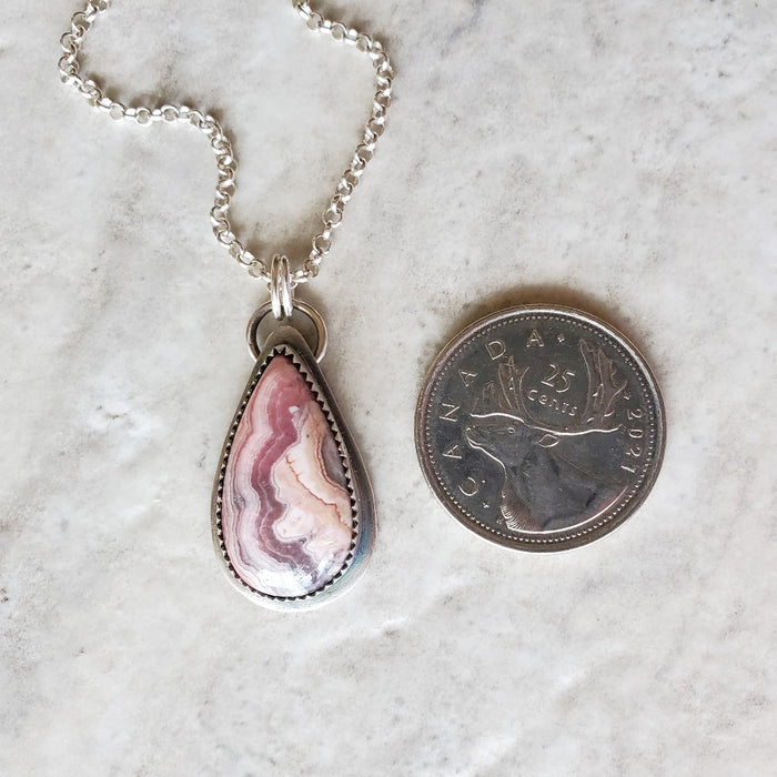 Rhodochrosite pendant necklace beside a quarter