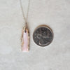 Pink opal nugget pendant necklace beside a quarter