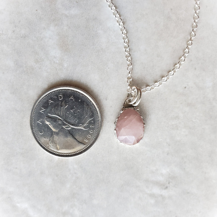 Necklace with a pink pendant next to a Canadian quarter on a light gray background