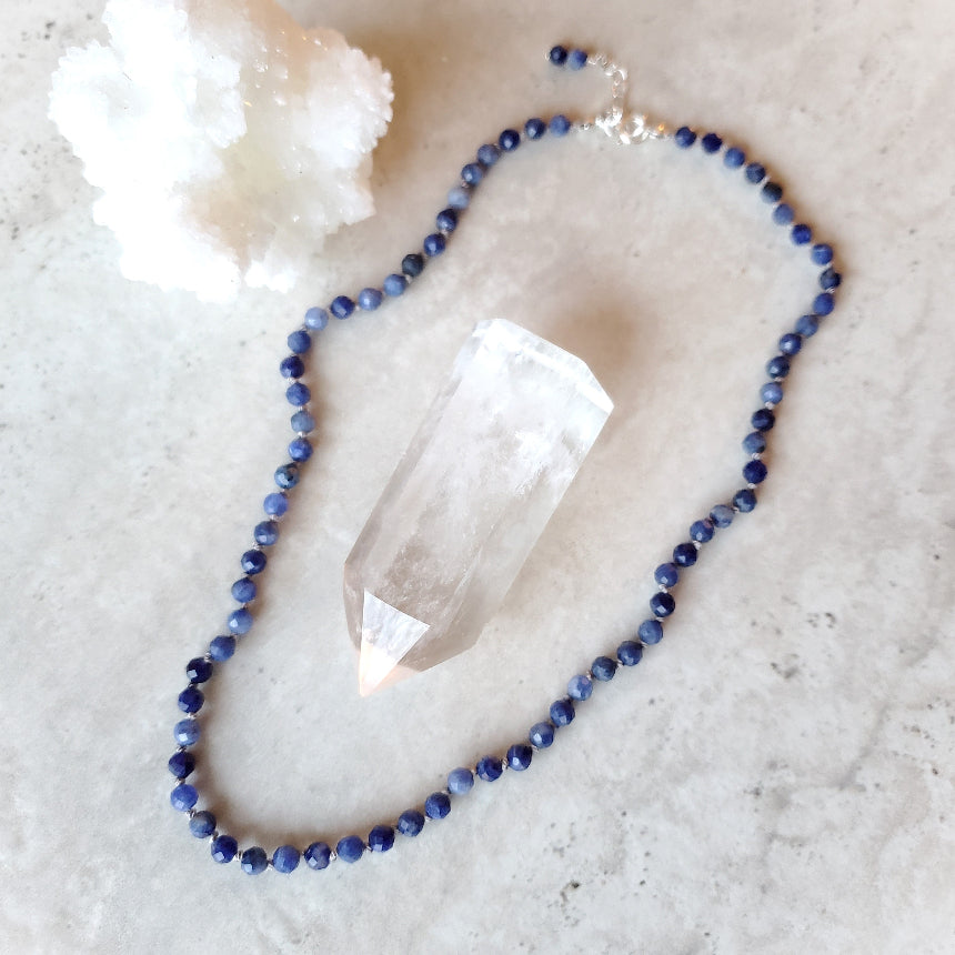 Faceted Sodalite necklace with a clear crystal on a light stone surface