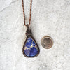 Sodalite copper wire wrap pendant beside a quarter