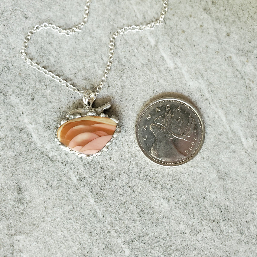 Imperial Jasper freeform pendant next to a Canadian quarter on a textured surface