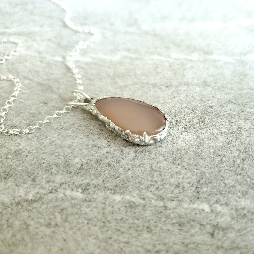 Necklace with a teardrop-shaped Peach Moonstone pendant on a textured surface