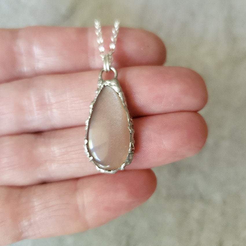 Teardrop-shaped Peach Moonstone pendant with silver chain held in hand 