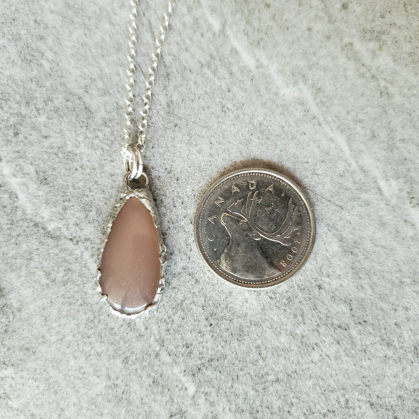 Peach Moonstone pendant next to a Canadian quarter on a gray surface