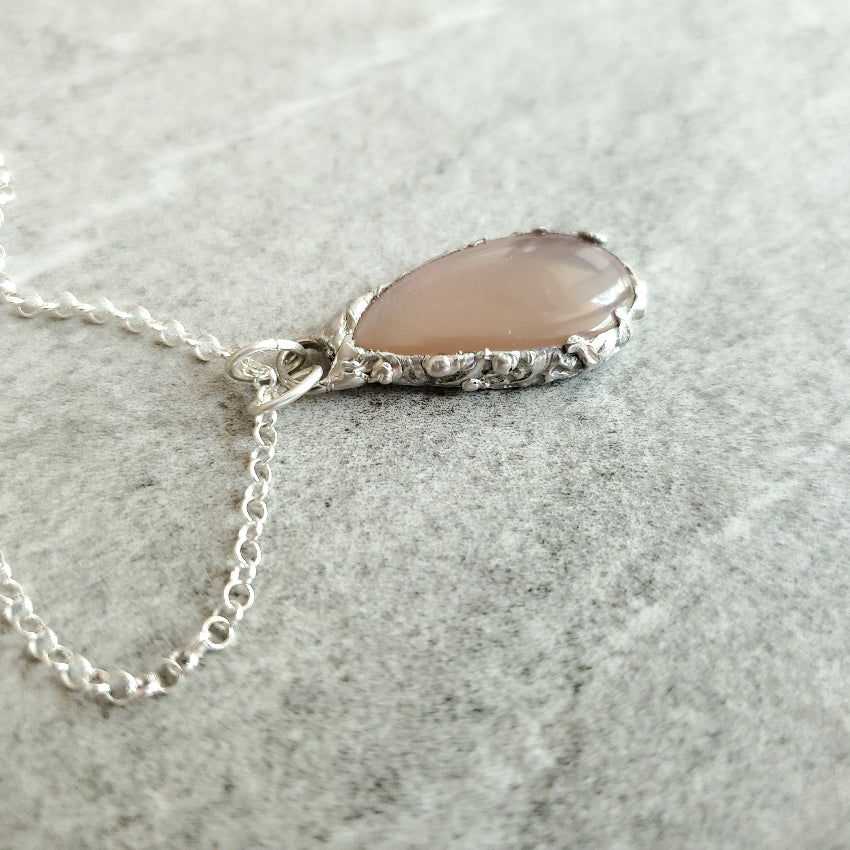 Necklace with a Peach Moonstone teardrop pendant on a gray surface