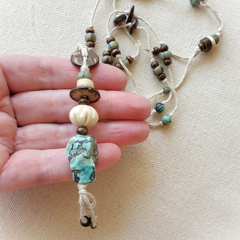 Beaded necklace with a large turquoise bead held by a hand on a beige background