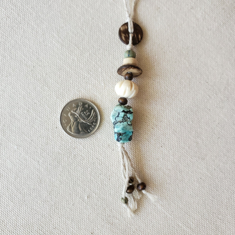 Beaded string with turquoise and white beads next to a coin on a light gray background