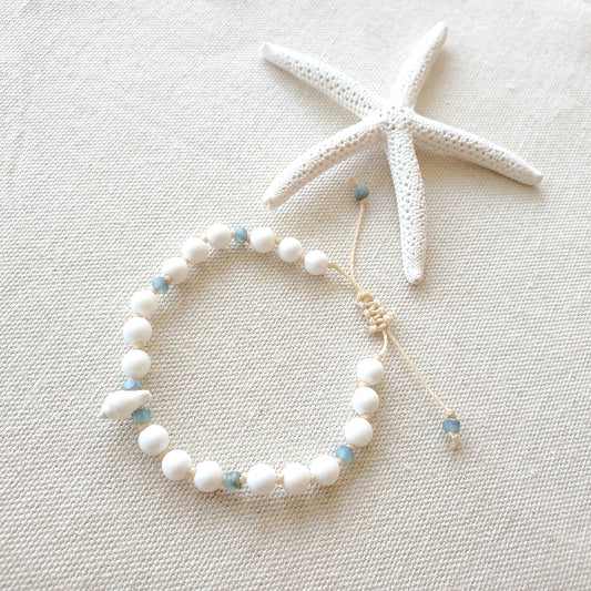 White shell beaded bracelet with small blue beads on a light beige fabric background with a starfish.
