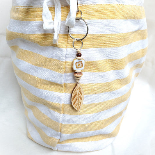 Yellow and white striped bag with a keychain featuring a leaf pendant on a white background